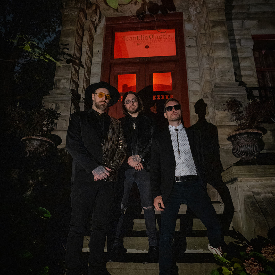 Three guys standing on the steps of a spooky building.